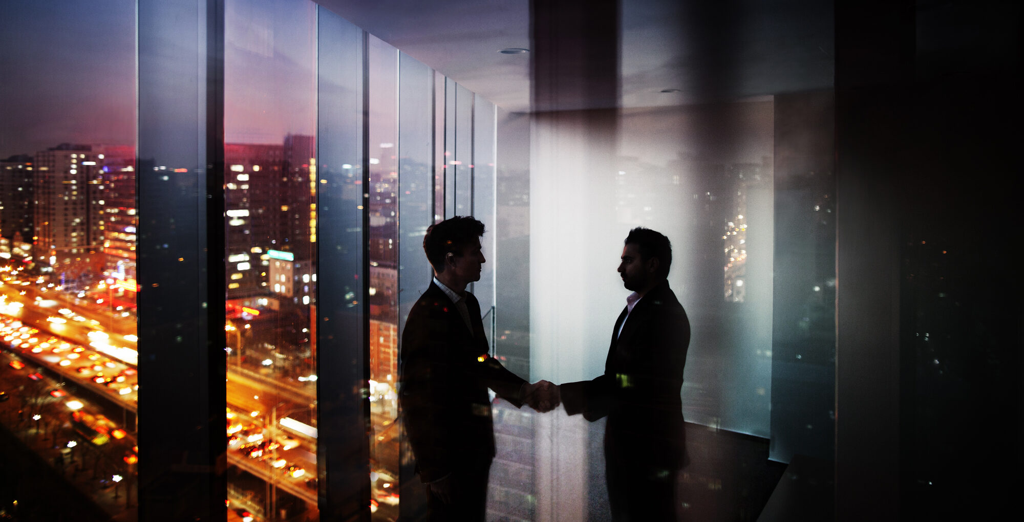 Businessmen shaking hands in office at night with city view